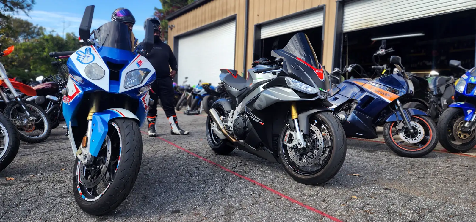 Motorcycle service Alpharetta riders use — blue and white GSX-R and silver Aprilia RSV4 outside the shop doors