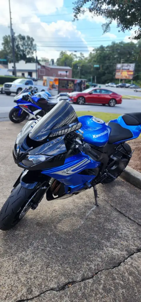 Blue Kawasaki Ninja motorcycle parked on pavement, with nearby trees and other vehicles in the background.