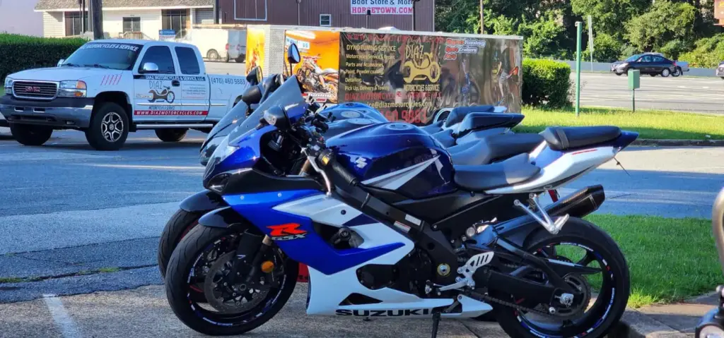 A blue and white Suzuki sport motorcycle is parked outside a trailer and truck in a parking lot.