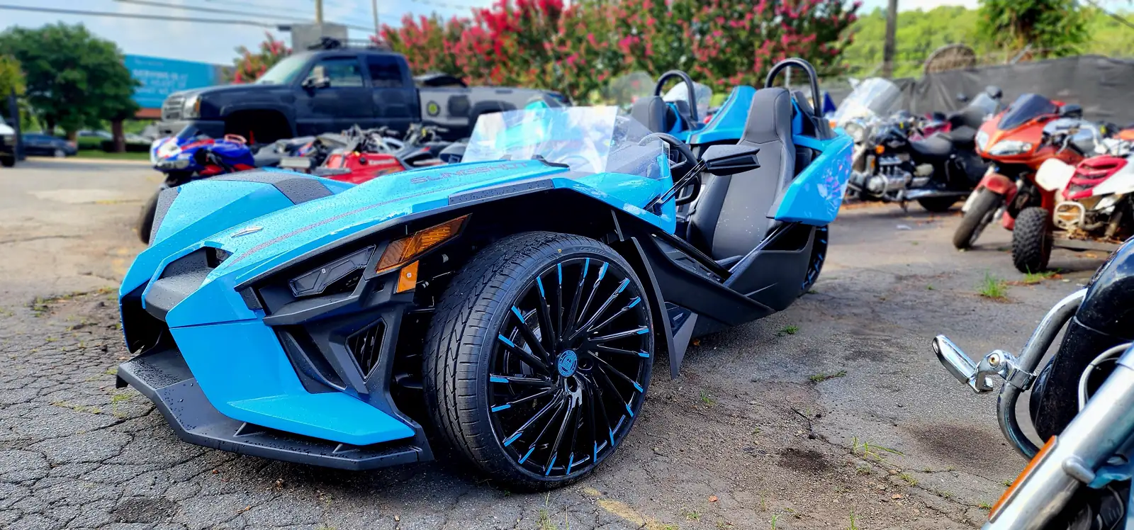 motorcycle transport Roswell — bright blue Polaris Slingshot three-wheeler parked in the shop lot with a pickup behind it