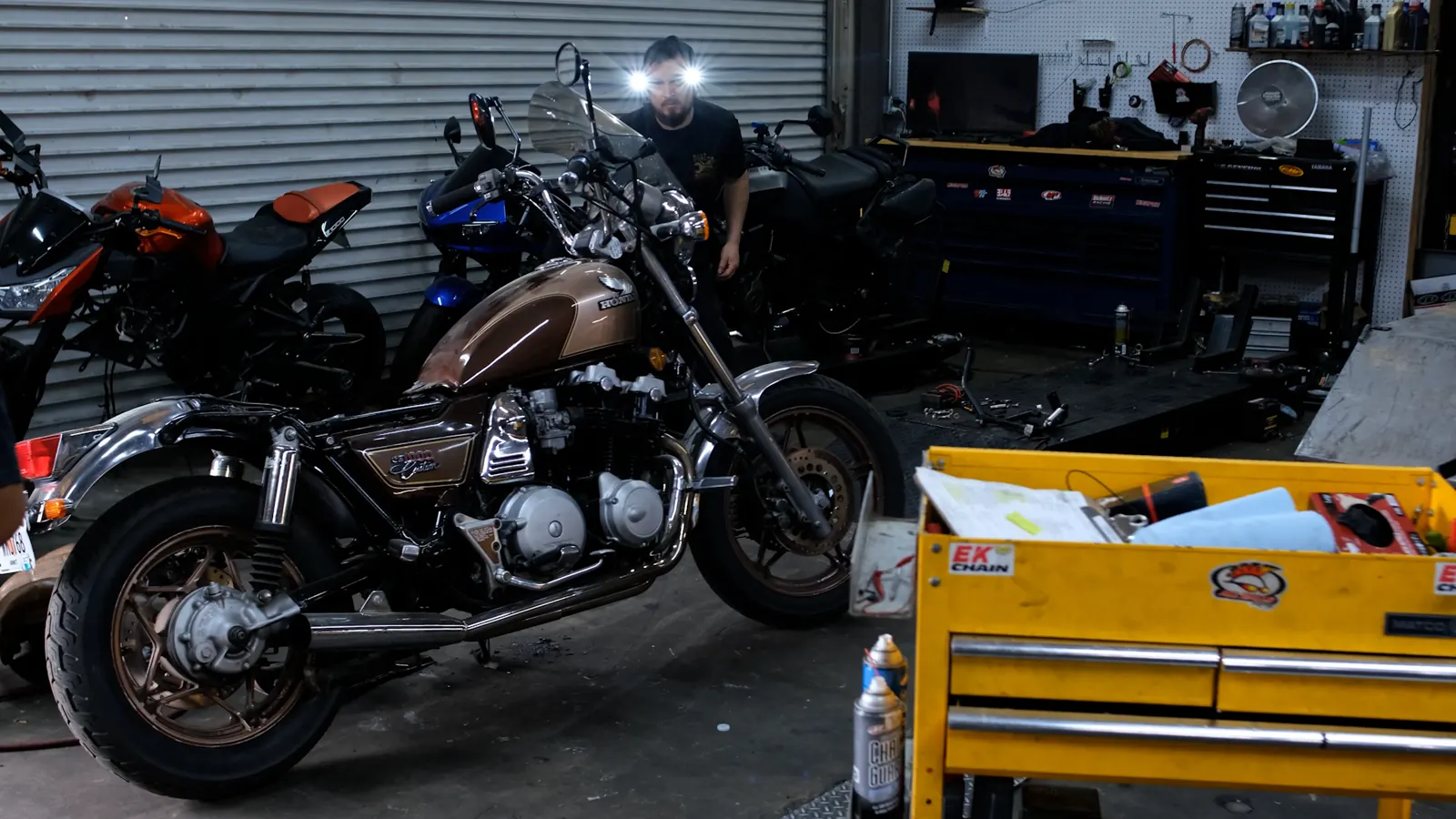 motorcycle transport Roswell — brown Honda cruiser on the shop floor with a technician in a headlamp behind it