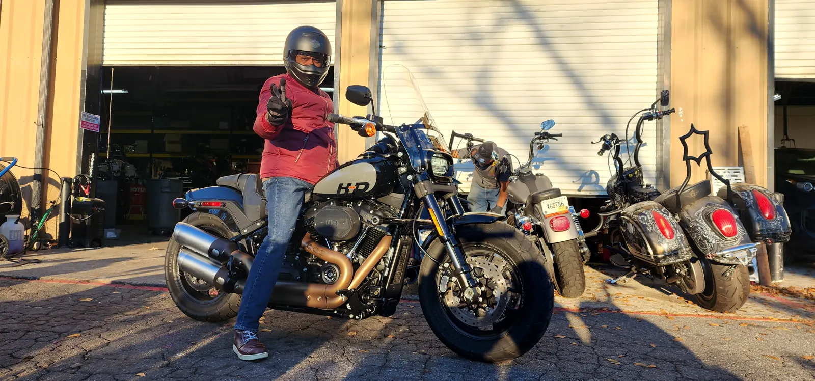 motorcycle transport Roswell — helmeted rider posing with a peace sign on a Harley Fat Bob outside the Diaz shop bays