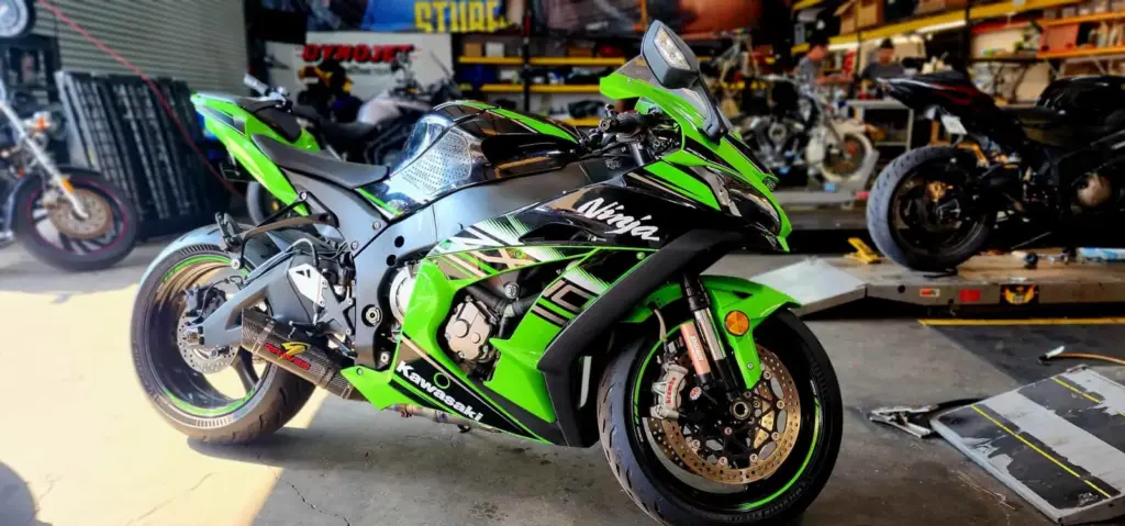 A green and black Kawasaki Ninja motorcycle is parked in a garage with tools and other bikes visible.