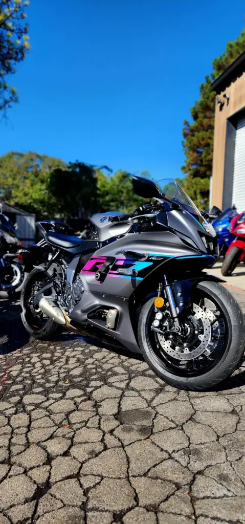 Sport motorcycle with a gray, blue, and purple design parked on a stone driveway under clear sky.