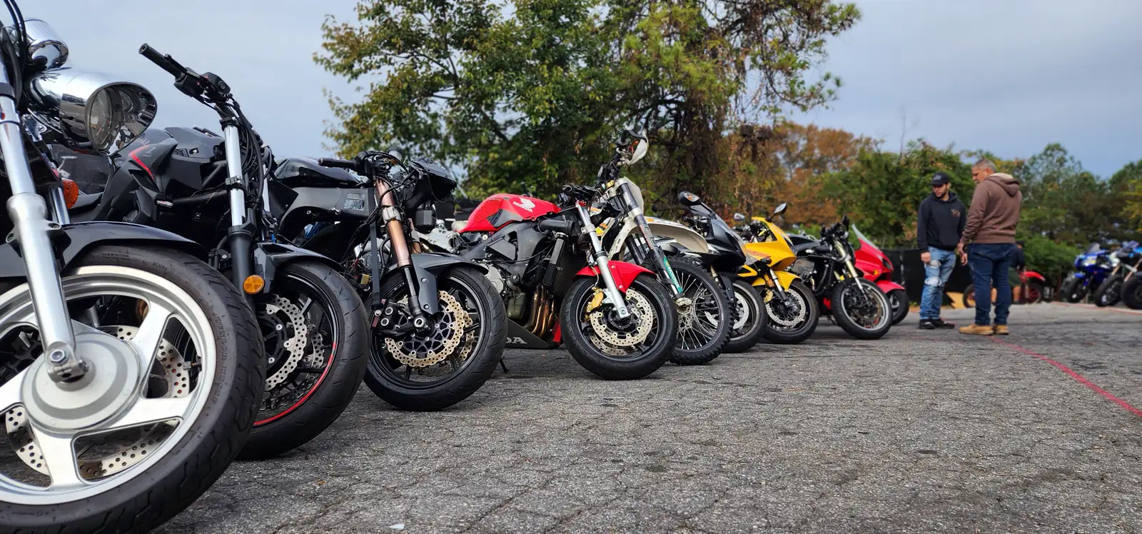 Best motorcycle service Cartersville — a long row of front wheels and forks from a dozen mixed bikes parked on asphalt.