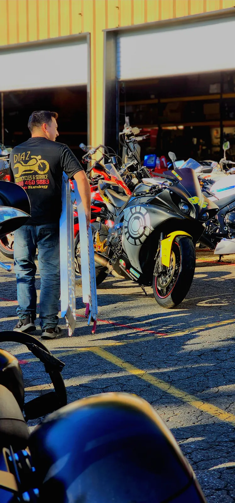 motorcycle transport Acworth — man in a Diaz Motorcycles t-shirt carrying aluminum loading ramps past a row of sportbikes