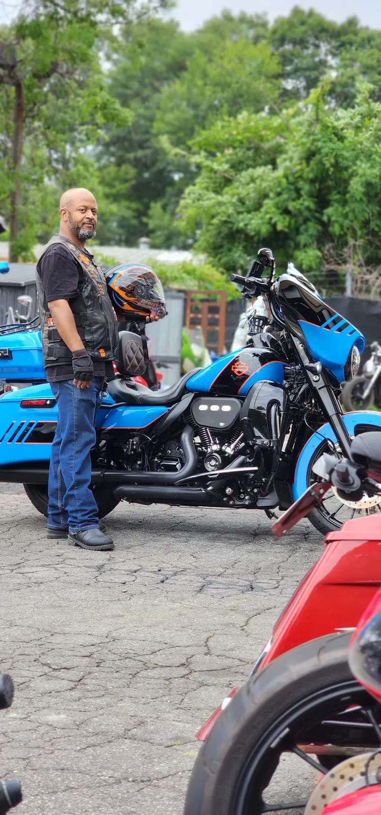 Motorcycle service Gainesville — man in a Harley leather vest holding an orange helmet beside a blue Harley bagger