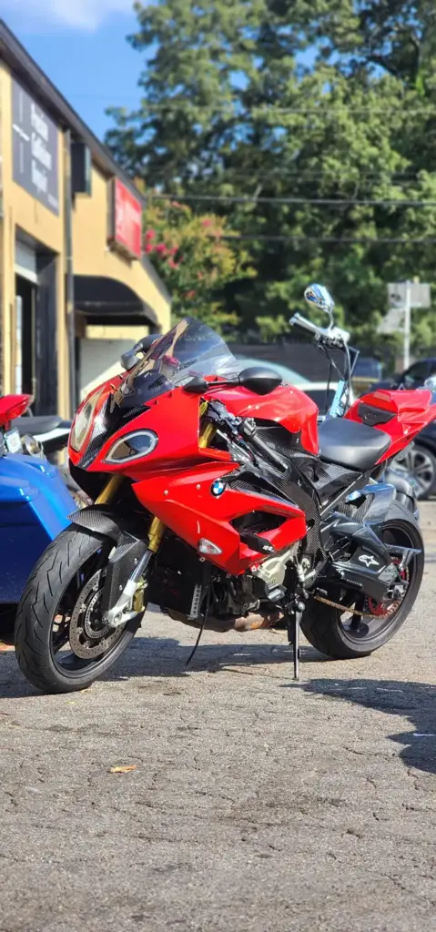 A red BMW sport motorcycle is parked on asphalt, with nearby trees and buildings in the background.