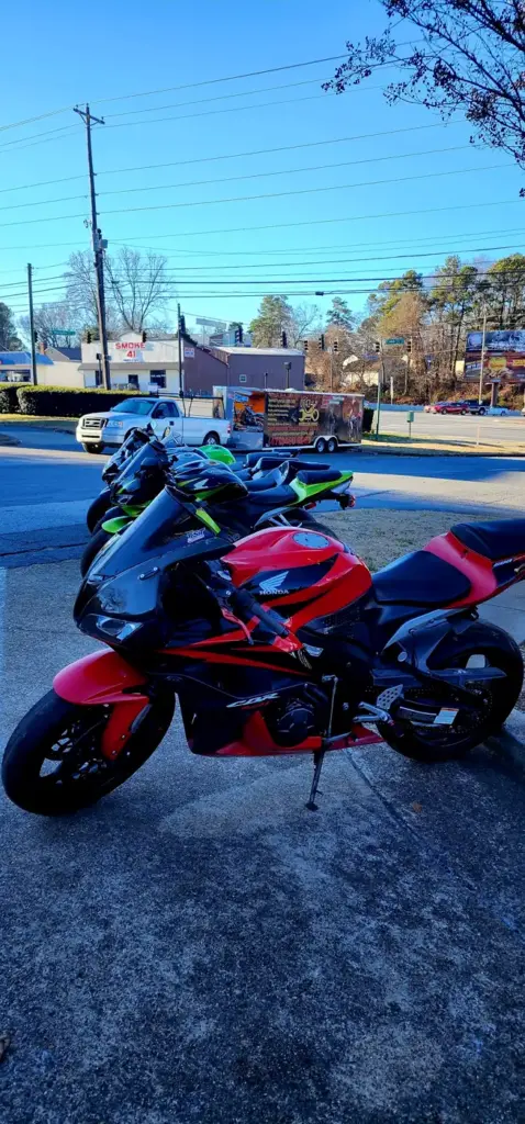 Four sport motorcycles are lined up on a sidewalk, with urban buildings and green trees in the background.