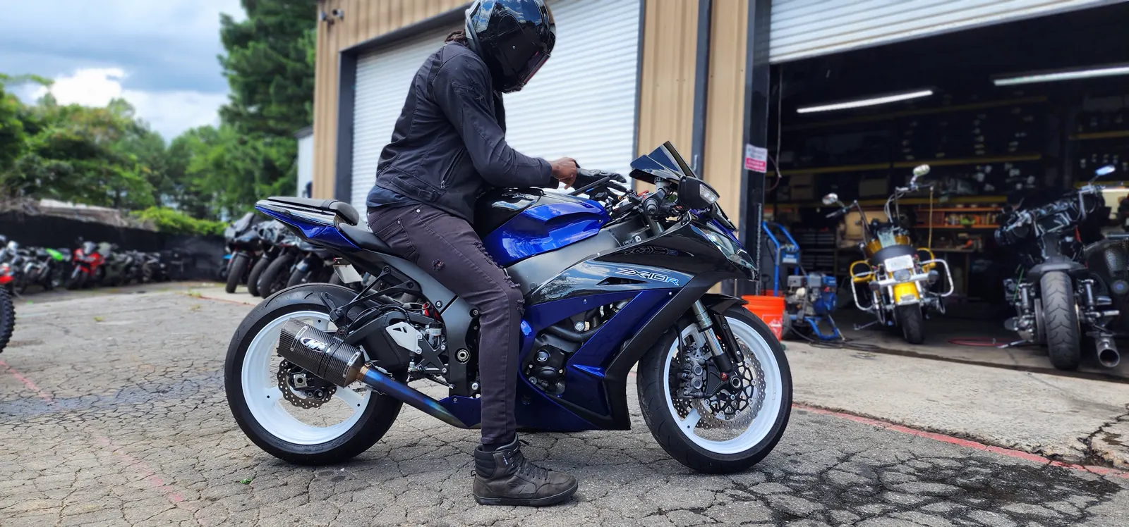 Powder Springs motorcycle pickup — rider in black jacket and helmet on a blue Kawasaki ZX-10R at the shop bays