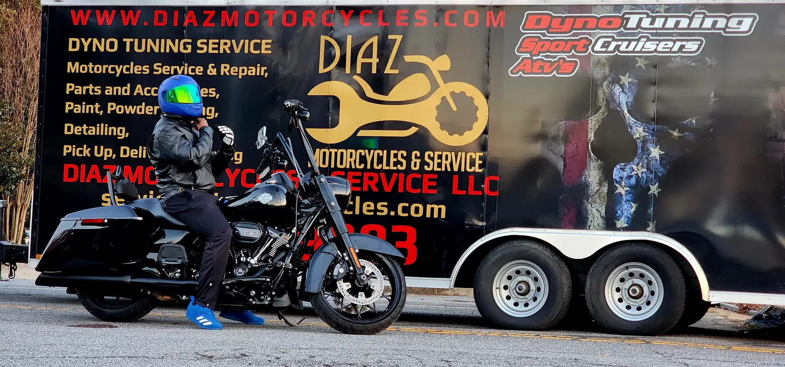 Powder Springs motorcycle transport — rider in blue helmet on a black Harley bagger by the wrapped Diaz trailer