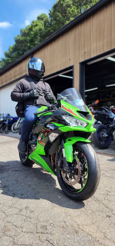 A person in black motorcycle gear and helmet rides a bright green sport bike parked before a garage door.