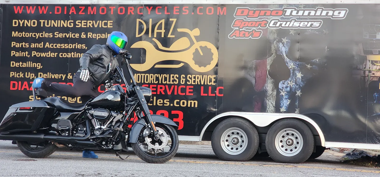 motorcycle service Newnan — rider in a green-blue helmet on a black Harley Road King passing the Diaz trailer