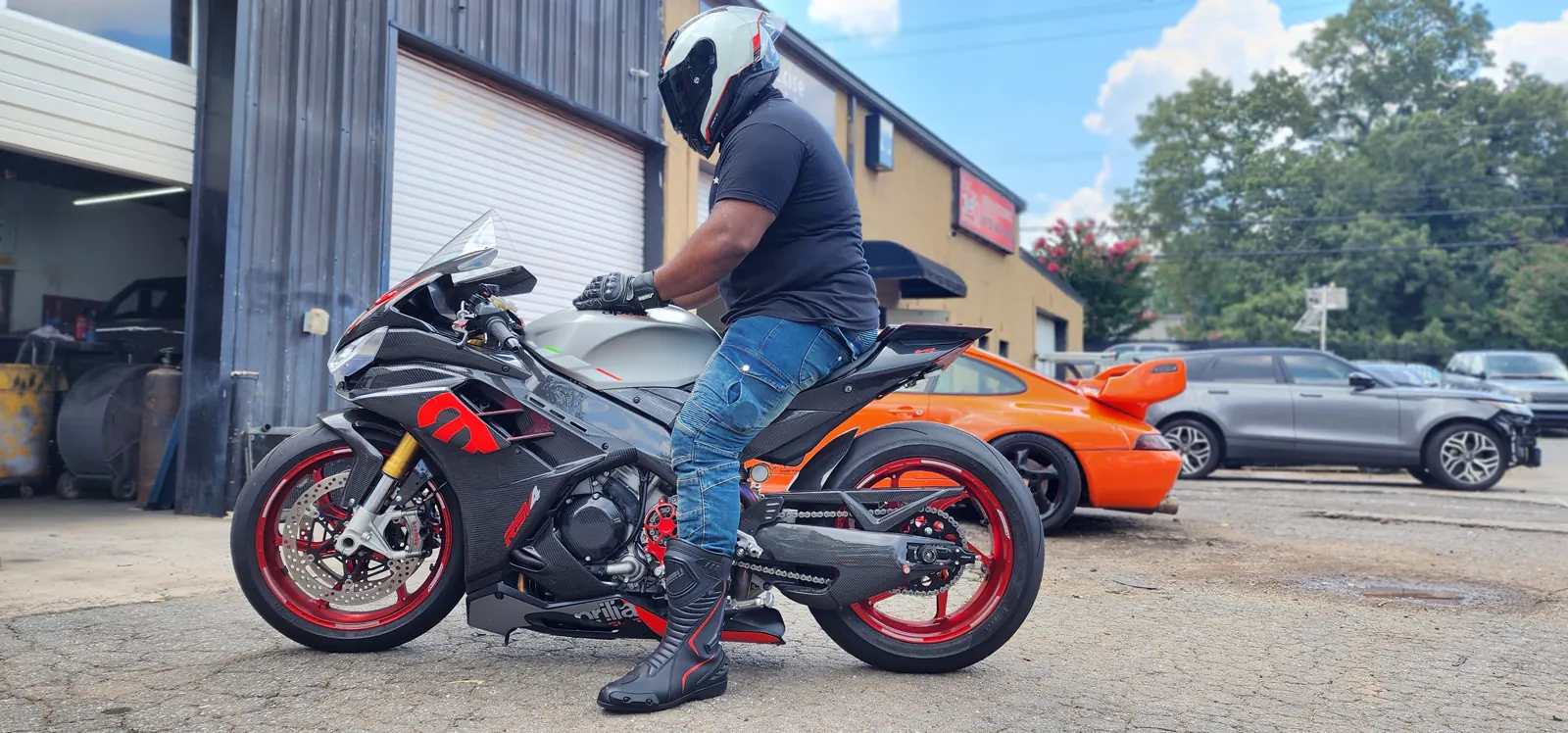 motorcycle service Newnan GA — rider in helmet, gloves and boots on a black and red Aprilia sportbike outside the shop bay