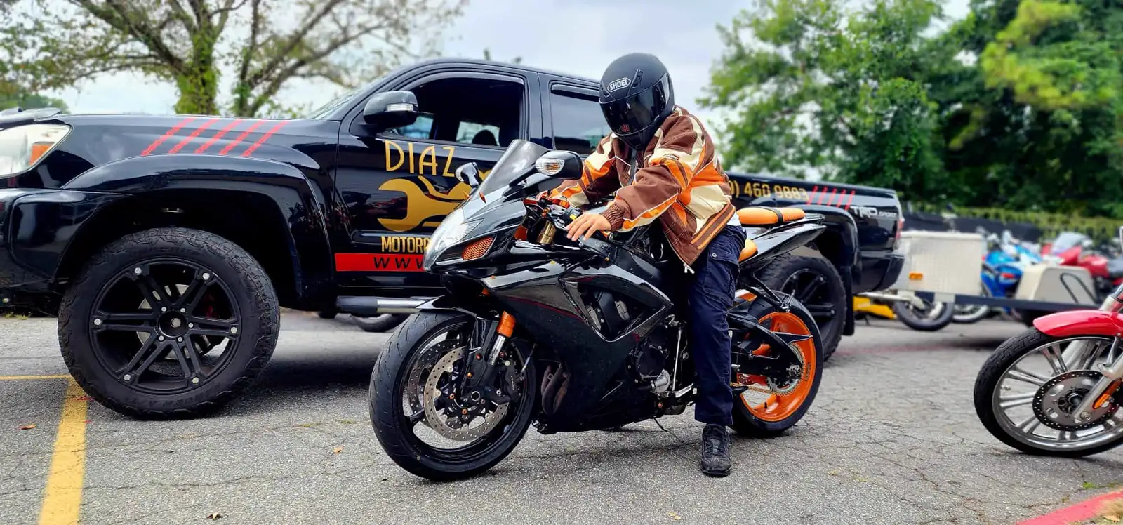 Dealer vs indie service near Newnan — rider in helmet and orange jacket on a black and orange Suzuki GSX-R by the Diaz truck