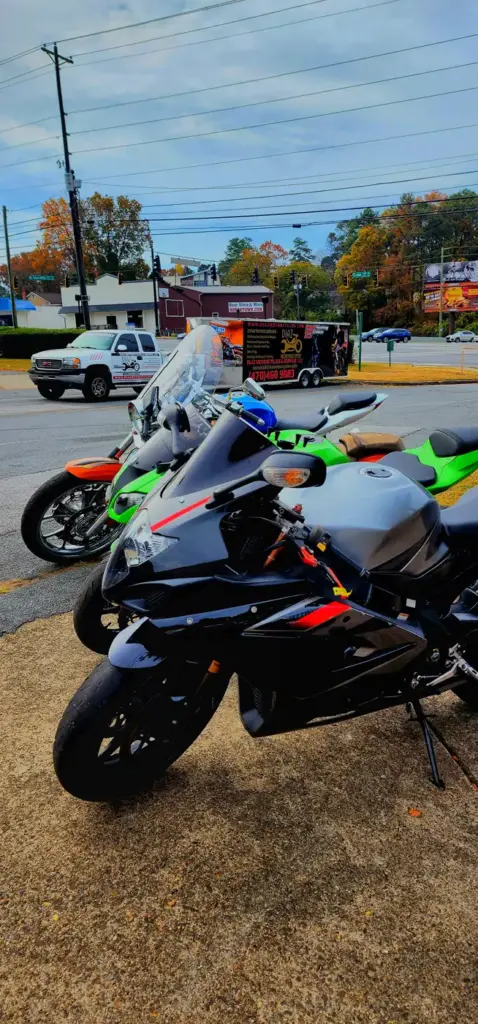 Two sport motorcycles parked on a city sidewalk near cars and vivid autumn trees lining the street.