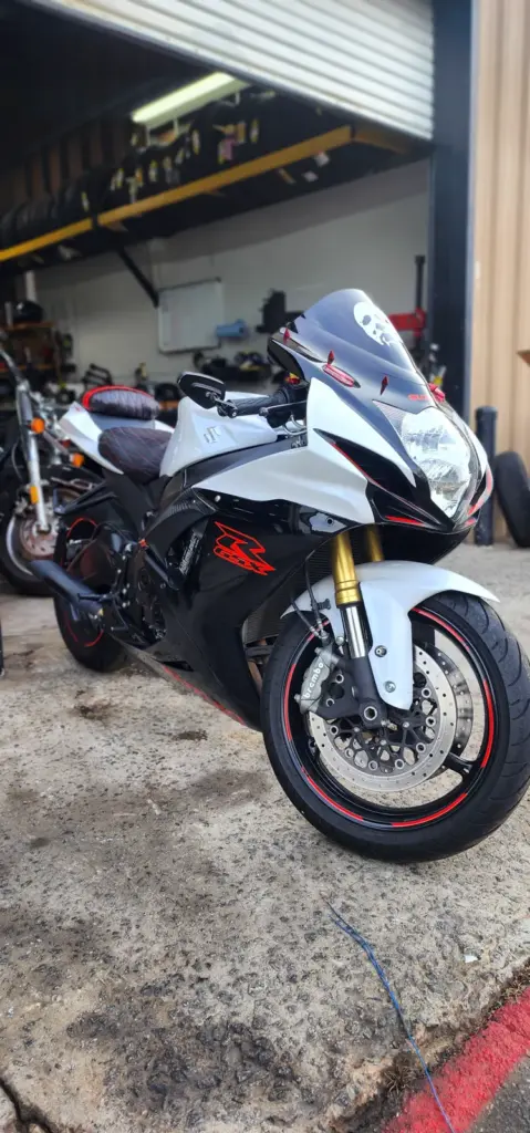 A black and white sport motorcycle is parked on concrete outside a garage with tools and other bikes visible.