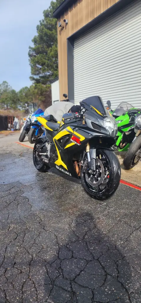 A yellow and black Suzuki sport motorcycle is parked on wet pavement, with other motorcycles behind it.