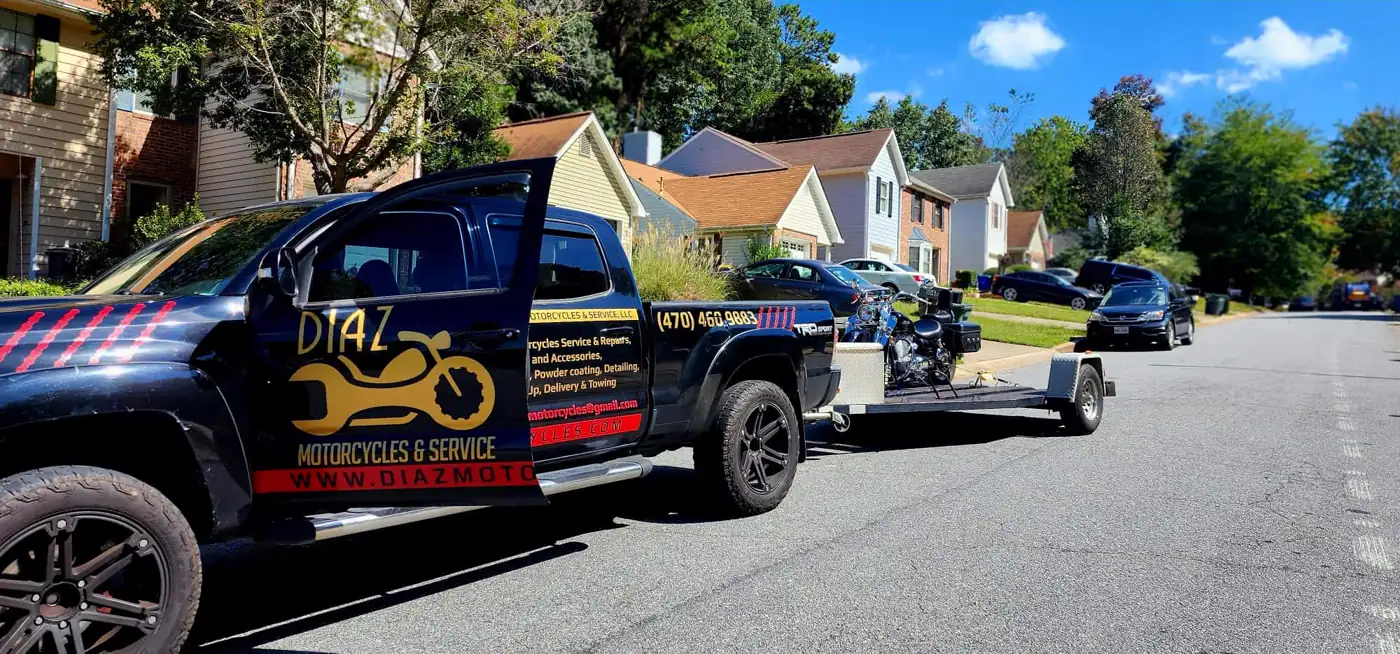 motorcycle transport Mableton — black branded Diaz Tacoma pulling an open trailer with a bike down a residential street