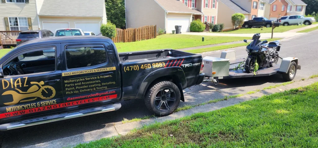 Black Diaz-branded Toyota Tacoma towing an open trailer with a sportbike strapped on, parked on a suburban street