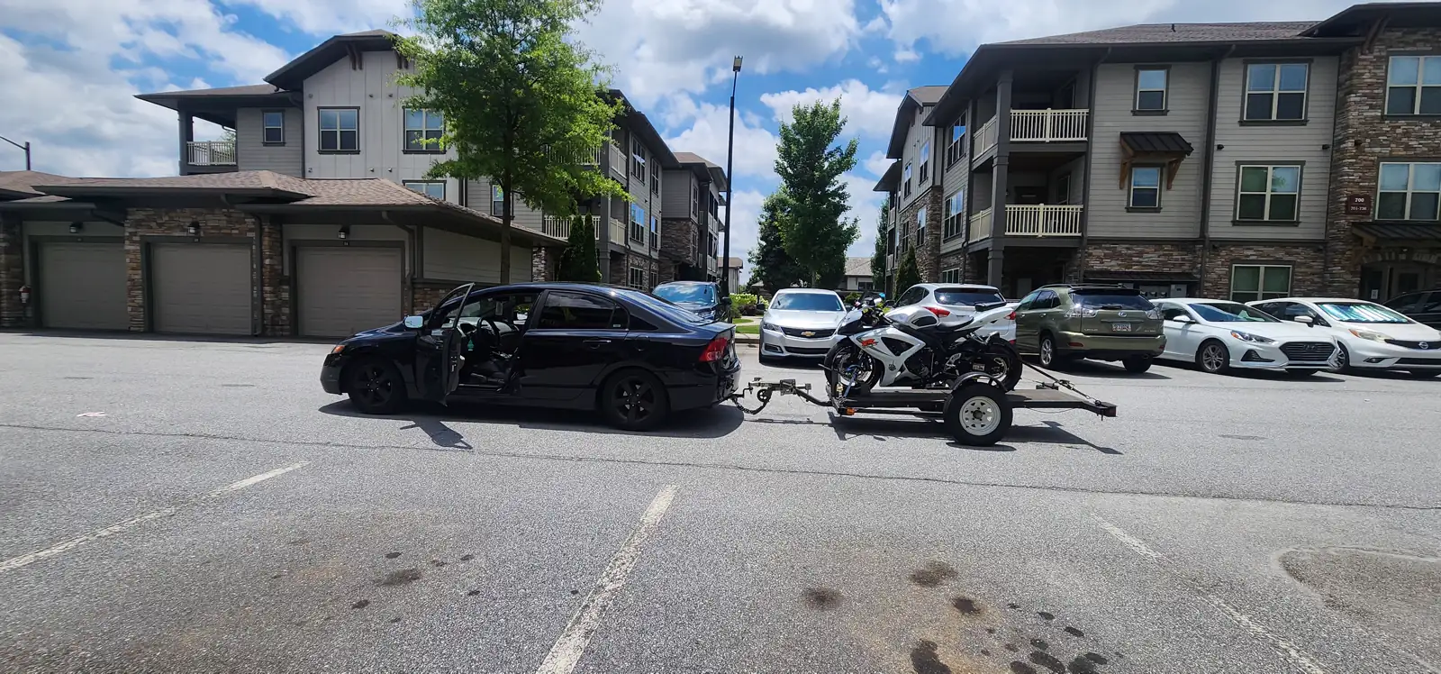 Motorcycle transport Acworth — black Honda Civic tows an open trailer with a white and red sportbike strapped on