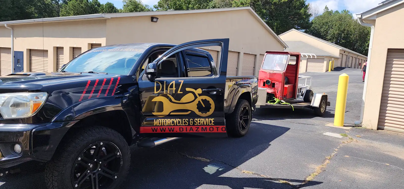 Motorcycle transport Mableton — Diaz Tacoma tows an open trailer with a red three-wheeler past storage units.