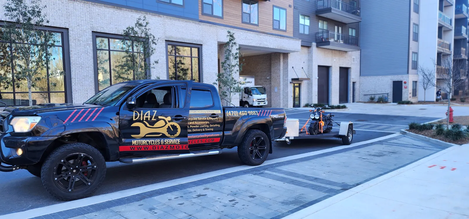 motorcycle transport cost Acworth — wrapped Diaz Tacoma hauling an orange cruiser on an open trailer