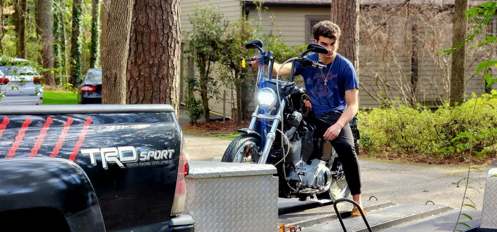 Close view of a young man mounted on a black Harley Sportster at the edge of the trailer ramp beside the Diaz Tacoma tailgate.