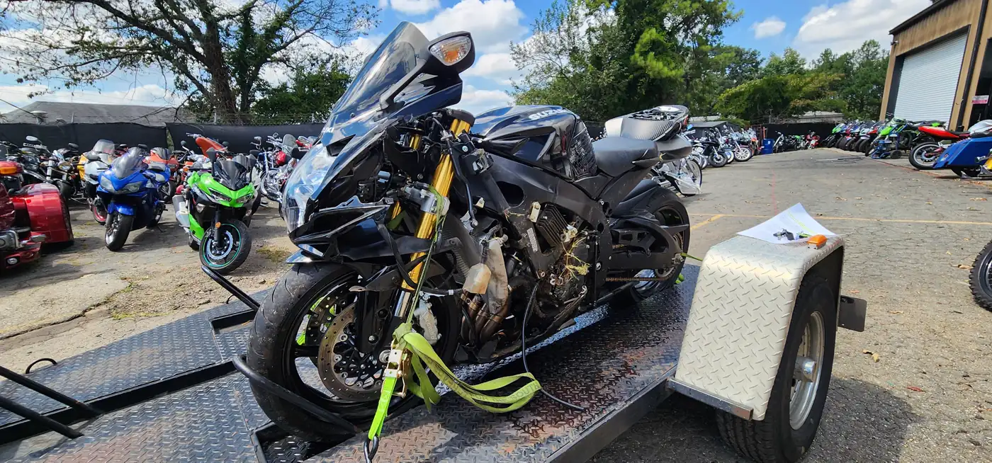 Motorcycle transport Woodstock — damaged black Suzuki GSX-R strapped on an open trailer with green straps