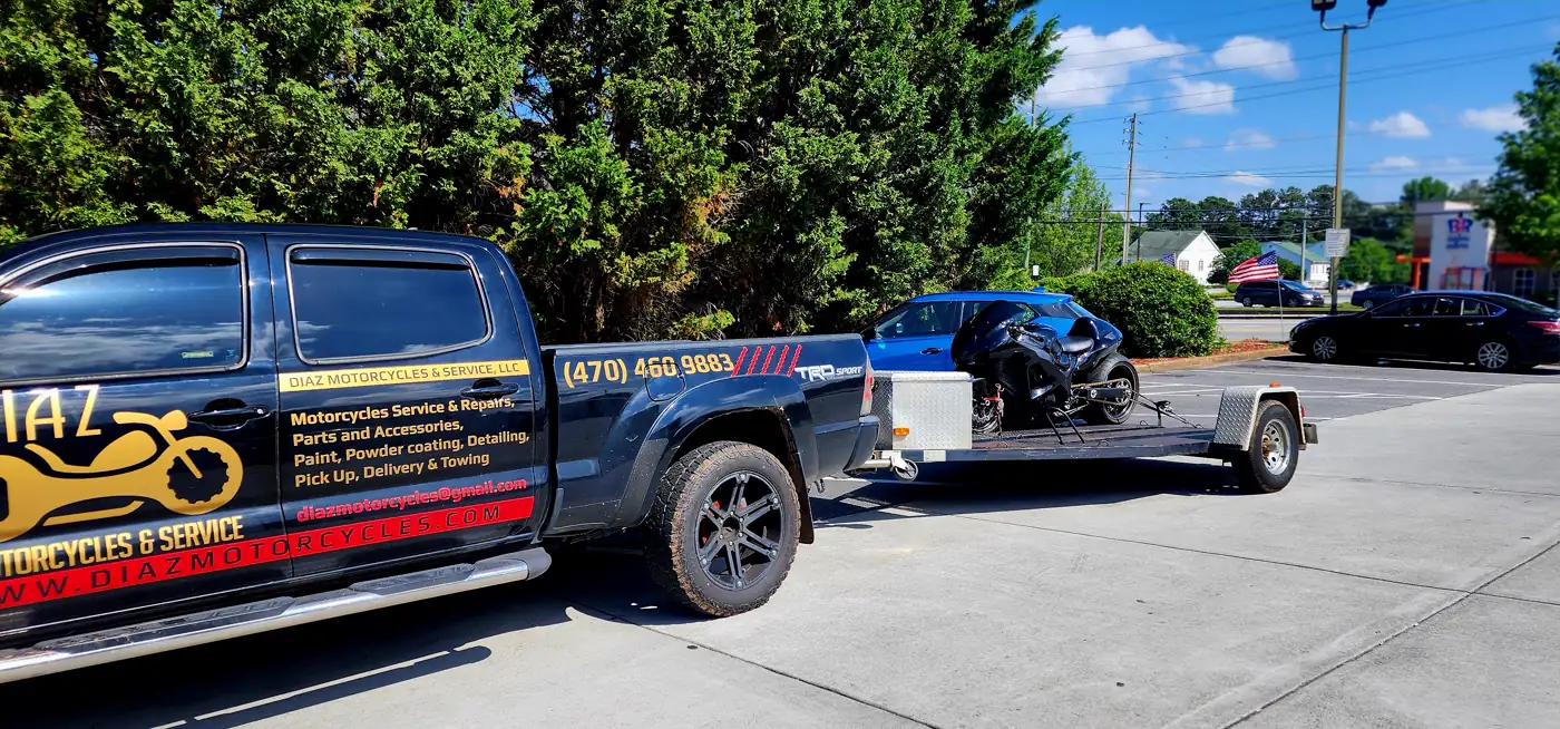 motorcycle pickup East Cobb — Diaz branded Tacoma with an open trailer carrying a black sportbike in a commercial lot