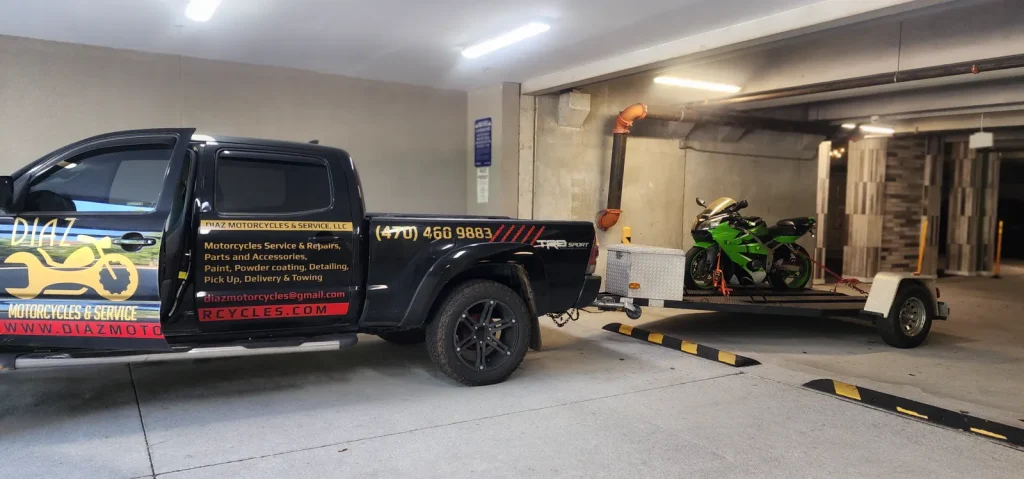 Diaz branded Tacoma and open trailer carrying a green Kawasaki Ninja inside a covered parking garage.