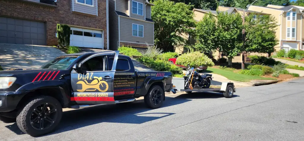 A black pickup truck towing a trailer with a motorcycle is parked on a suburban street near houses.
