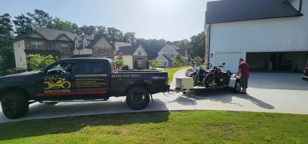 Diaz Tacoma and open trailer loaded with two cruisers backed into a suburban driveway while a customer in a red shirt stands at the trailer.