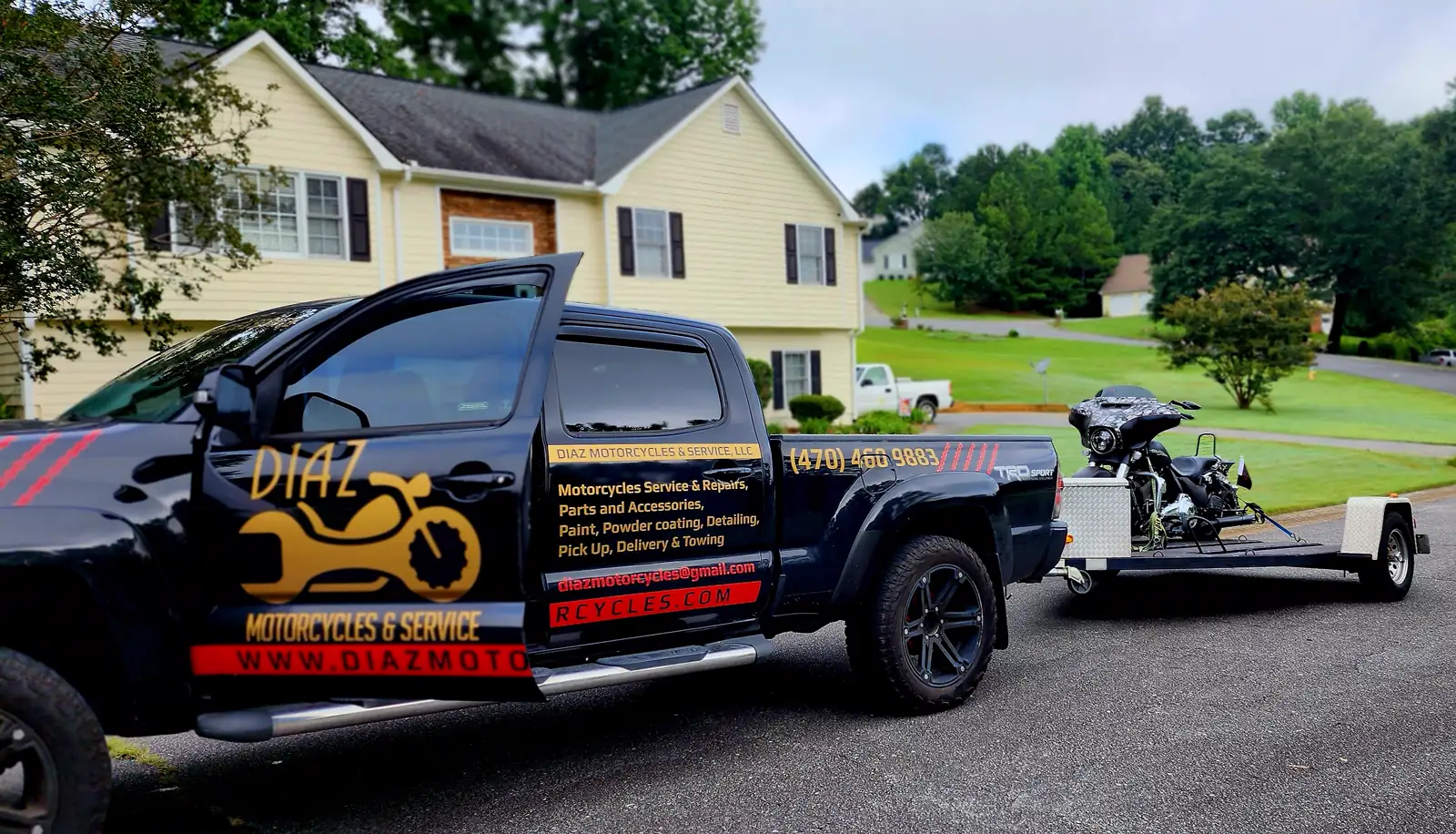 Open transport Woodstock — Diaz-wrapped black Toyota Tacoma towing a bagger out of a residential driveway