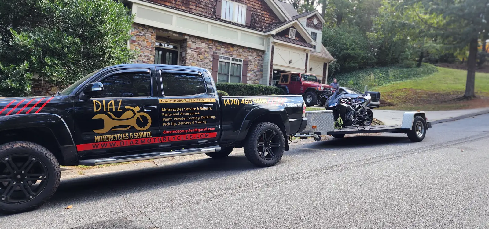 transport company East Cobb — Diaz-wrapped black Tacoma towing an open trailer with a black sportbike by a brick home