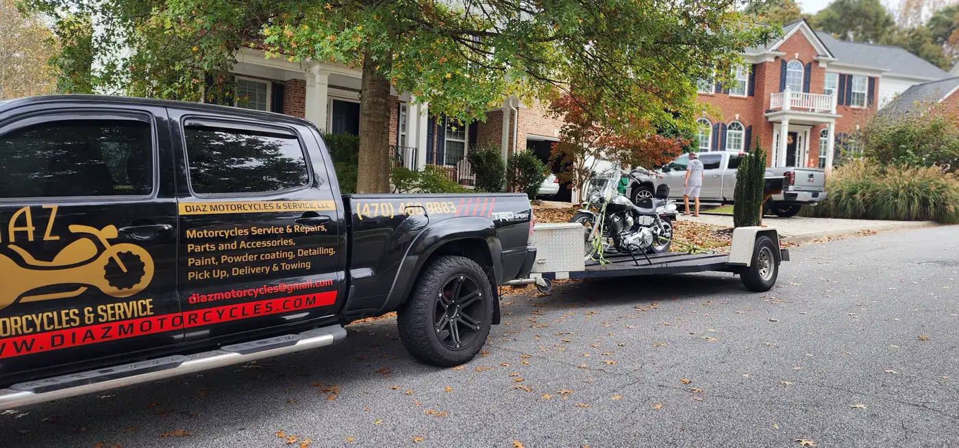 motorcycle transport Canton — Diaz-wrapped Tacoma towing an open trailer with a chrome Harley cruiser on a fall street