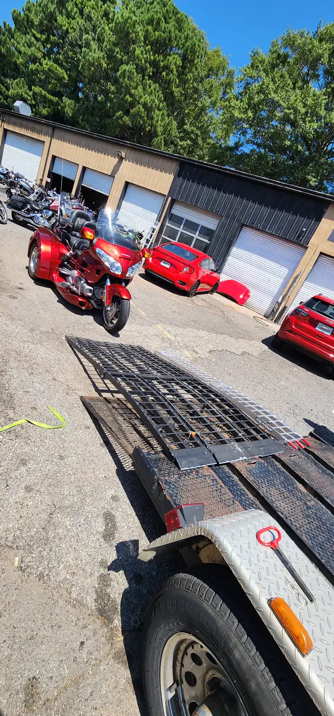 Motorcycle transport Acworth — empty open trailer with folding ramp and a red Honda Gold Wing trike by the shop bays