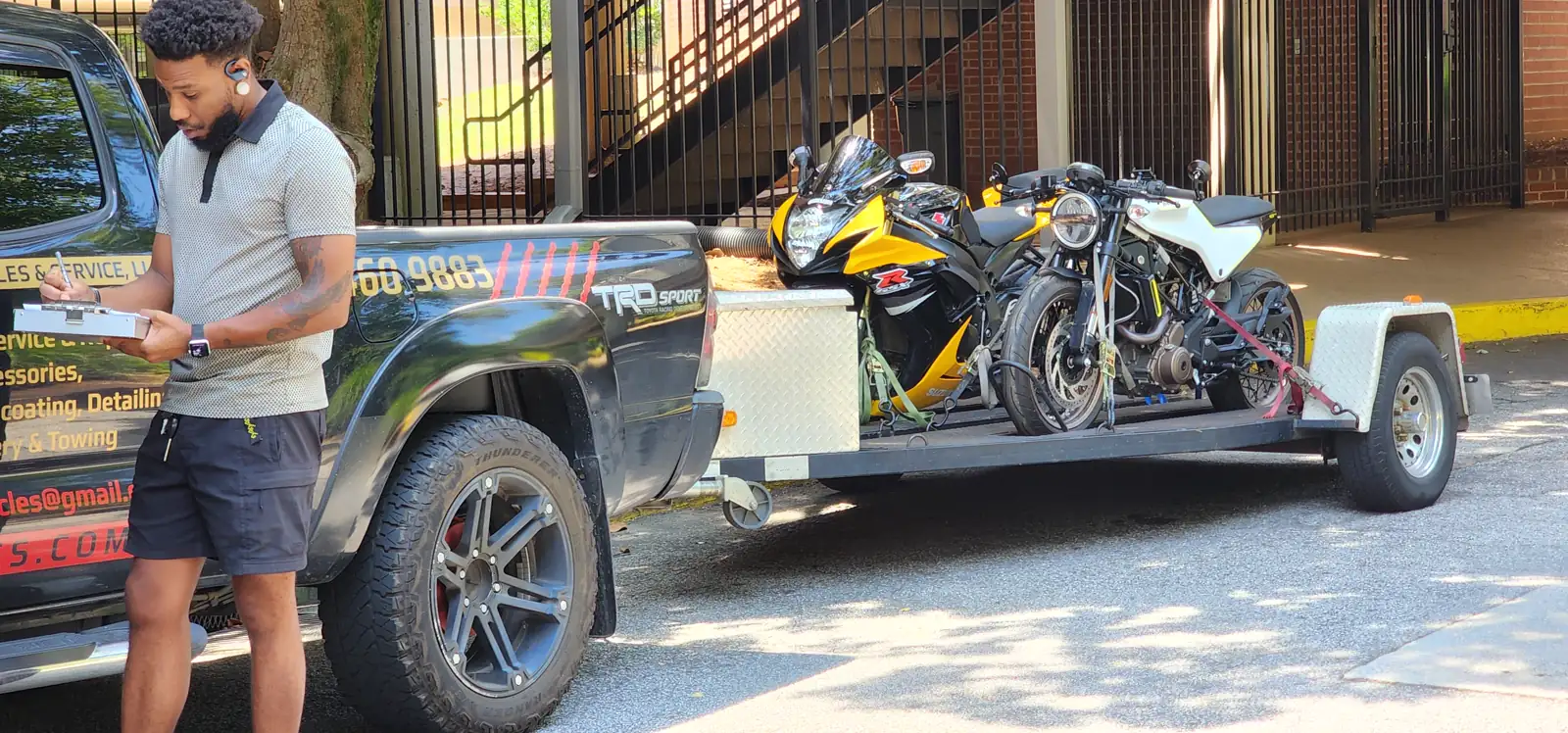 Motorcycle transport Kennesaw — man writing pickup notes beside the Diaz trailer loaded with a yellow GSX-R
