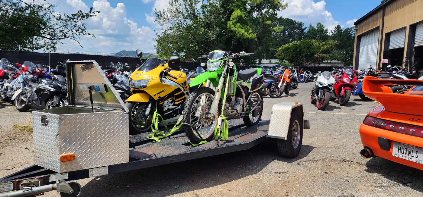 motorcycle transport Powder Springs — open trailer with a green Kawasaki dirt bike and yellow Honda CBR strapped down