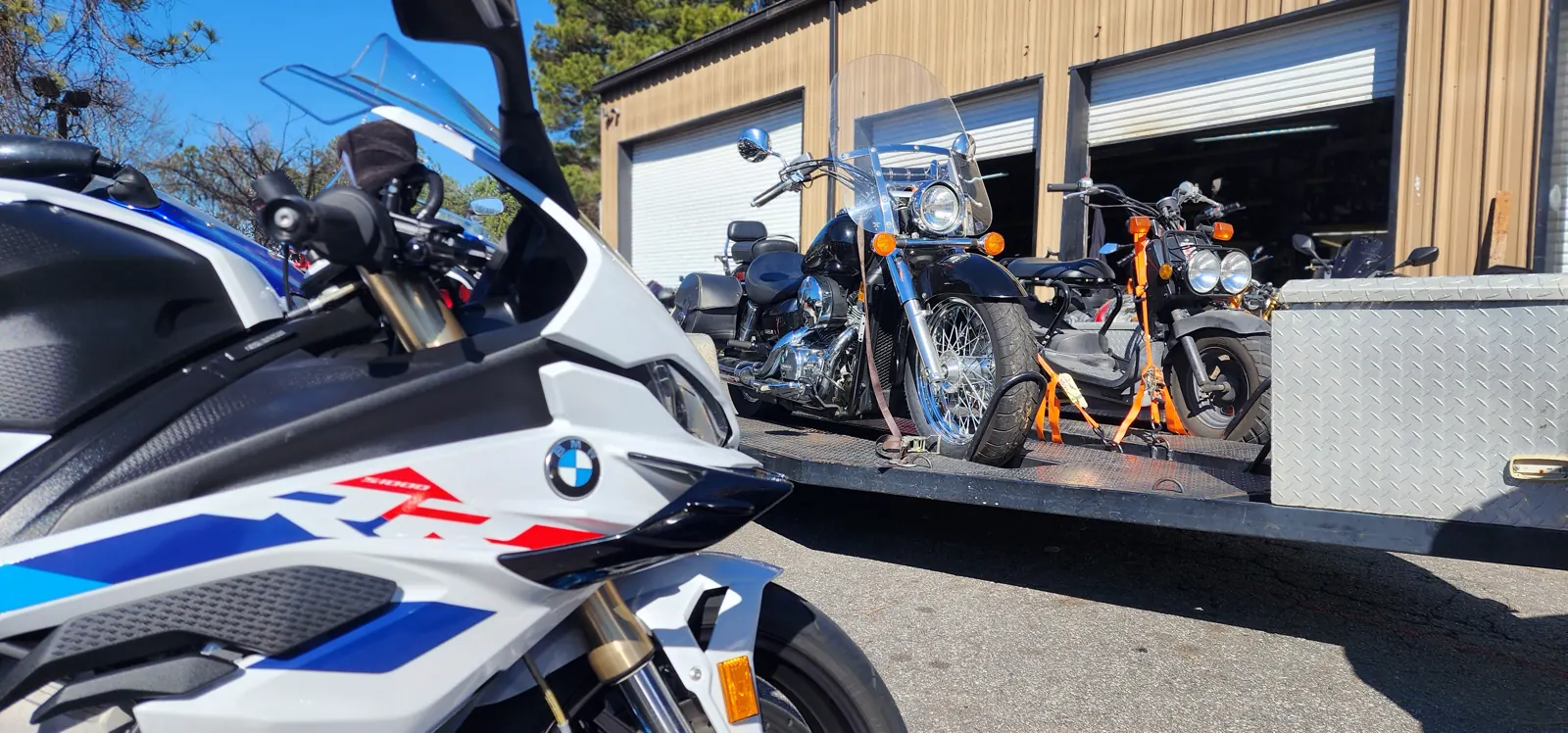motorcycle transport Smyrna — chrome Harley softail and a second bike strapped on an open trailer, BMW S1000RR in front