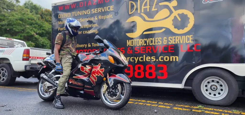 A helmeted person sits on a black motorcycle next to a van with Diaz Motorcycles & Service branding.