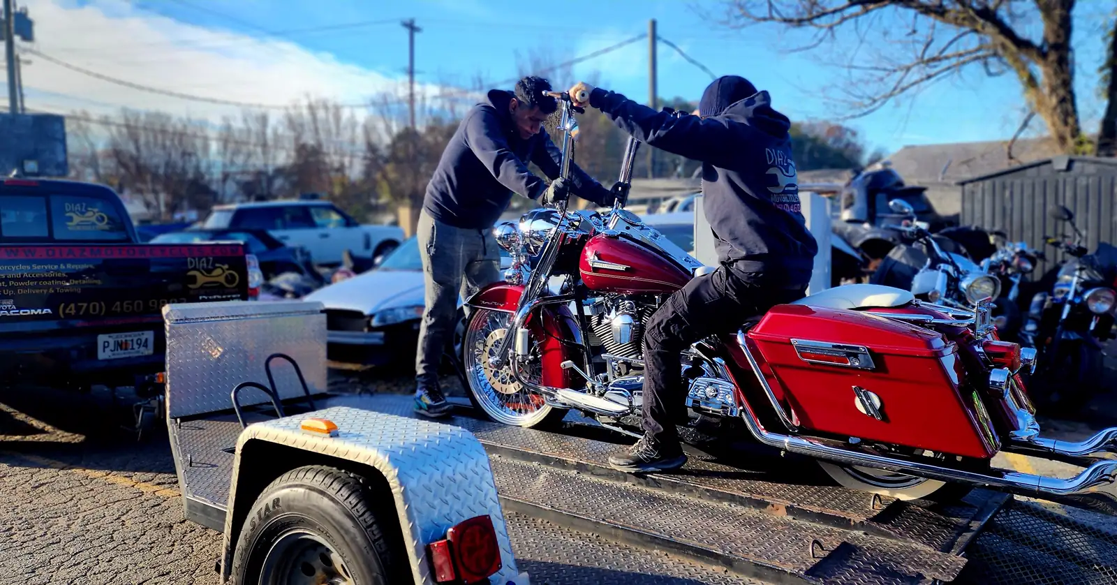 enclosed vs open transport Roswell — two men in Diaz hoodies loading a red Road King behind the branded pickup