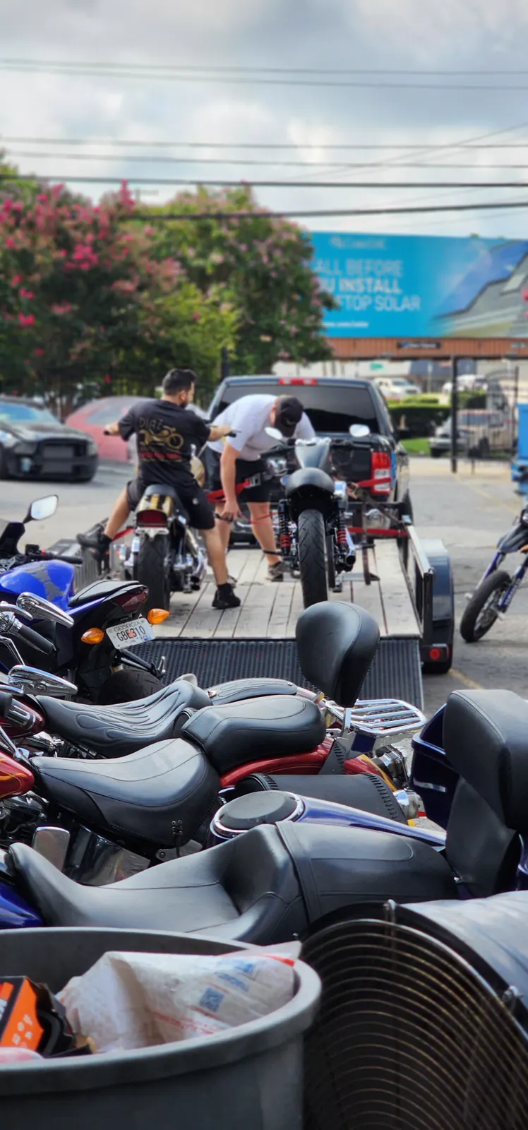 shipping cost Powder Springs — two men, one in a Diaz tee, rolling sportbikes onto an open flatbed trailer