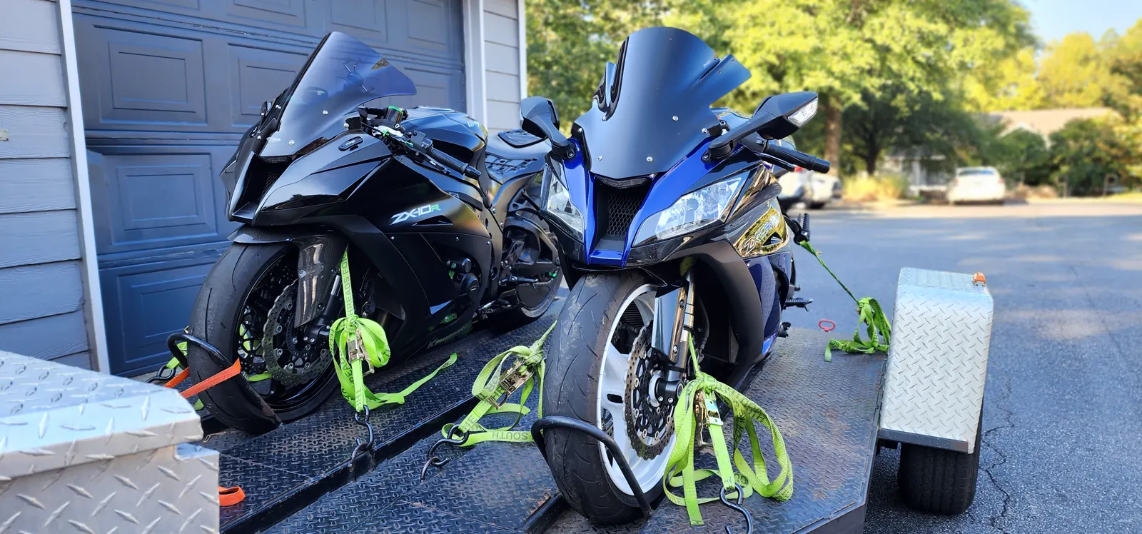 enclosed vs open transport Roswell — black Kawasaki ZX-10R and blue Yamaha R6 strapped on an open trailer