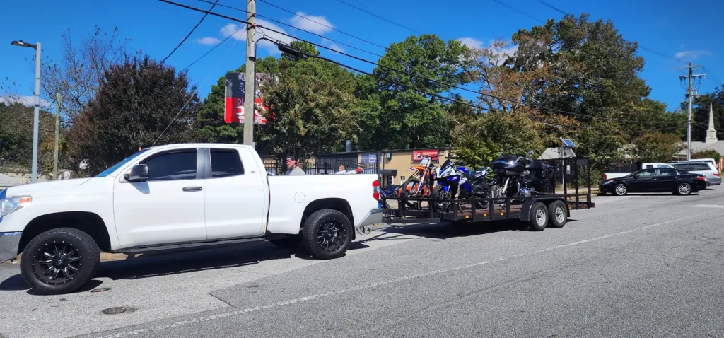 White Toyota Tundra towing a long dual-axle open trailer loaded with several dirt bikes and a bagger on a street