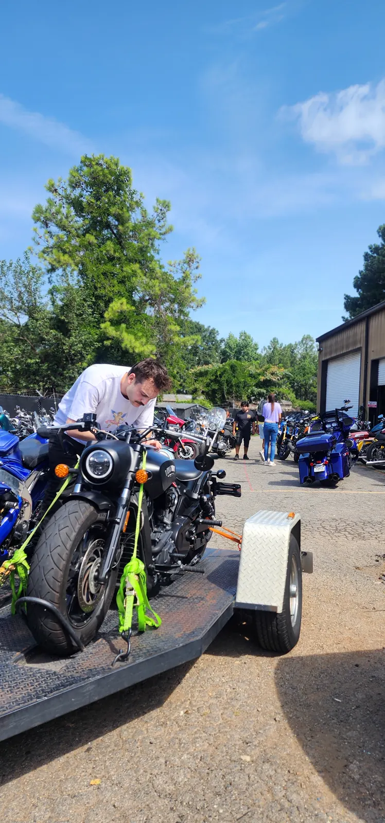 motorcycle transport Acworth — worker leaning over a black Indian Scout Bobber strapped to an open trailer with bikes behind